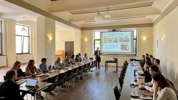 Une salle de conférence équipée d’une longue table, de chaises, d’un écran de projection et d’un présentateur.