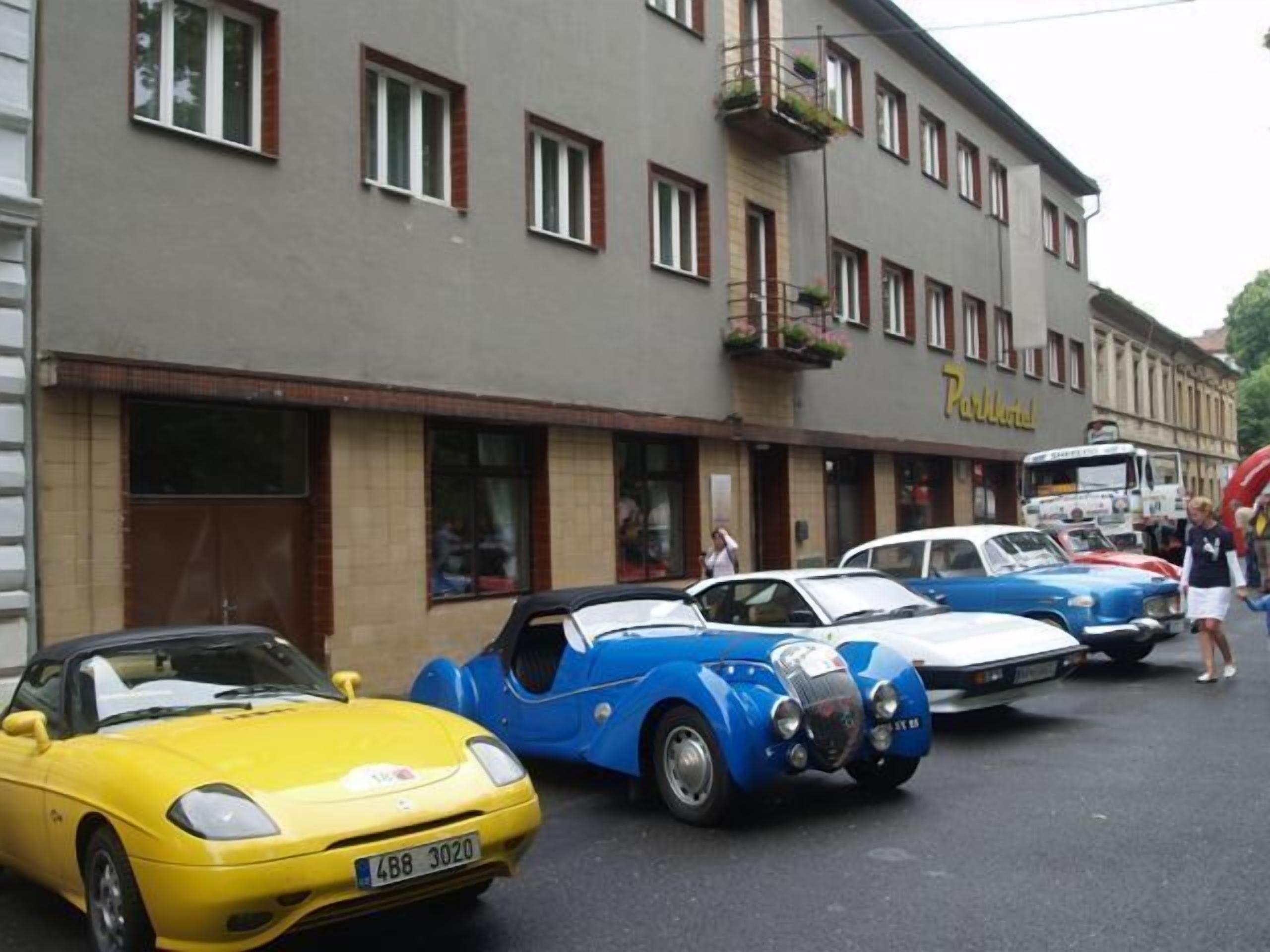 Eine Reihe klassischer Autos vor einem Gebäude, an dem ein Schild mit der Aufschrift 'Parkhotel' hängt.