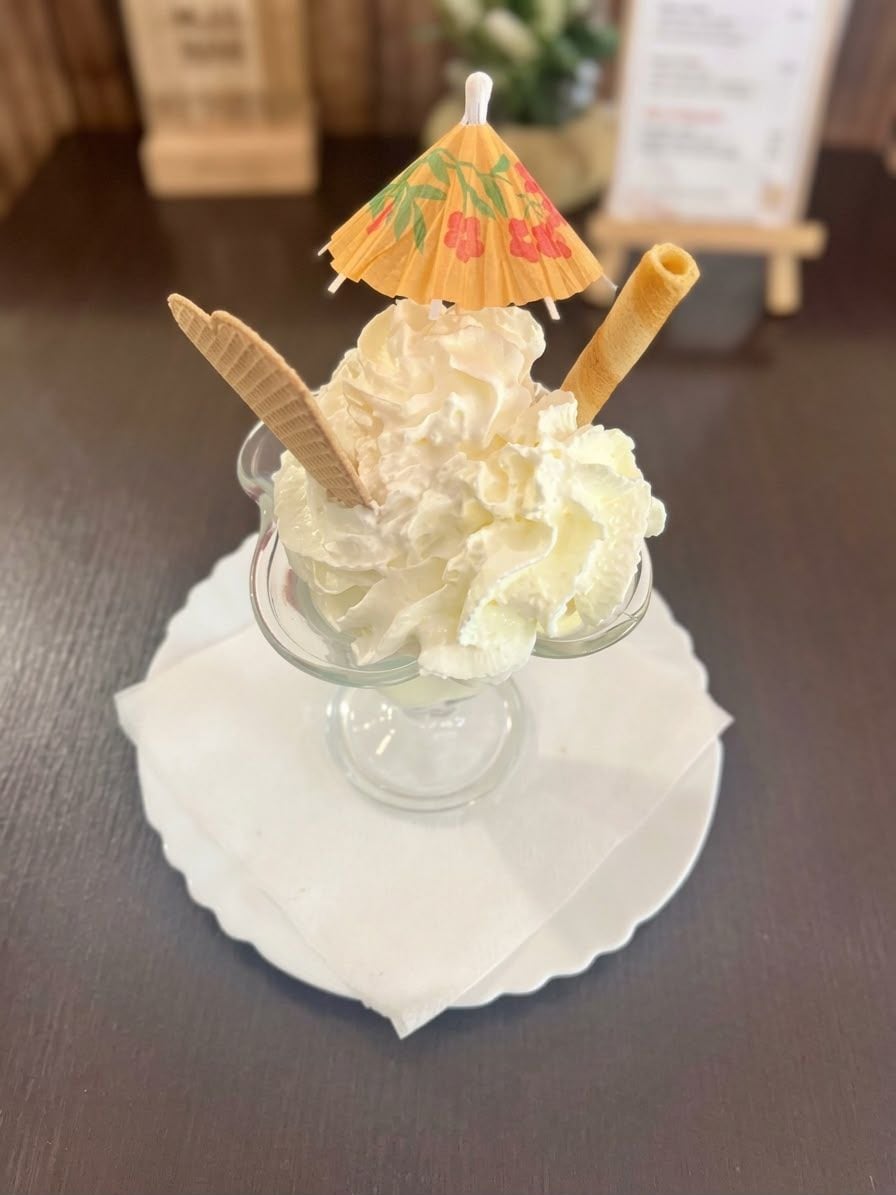 Un dessert composé de crème fouettée et d’un cornet de gaufre, servi dans un plat en verre transparent agrémenté d’un petit parapluie décoratif.