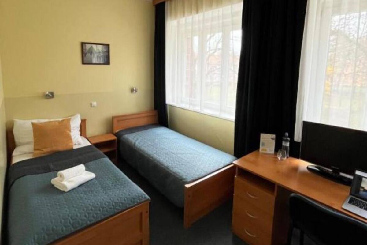 A hotel room with two beds, a desk, a chair, a TV, and a window with curtains.