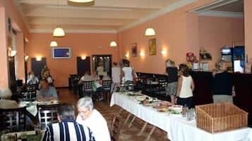 A dining area with tables set for meals, people seated and standing, and a buffet line.
