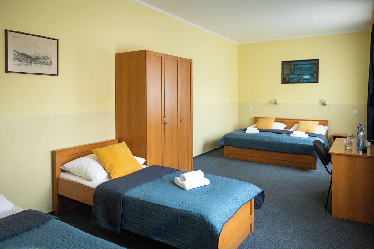 A hotel room with two beds, a wardrobe, a desk, and a painting on the wall.