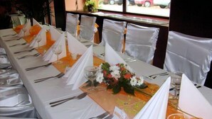 Een lange eettafel met witte tafellinnen, bestek en glazen, gedekt voor een maaltijd.