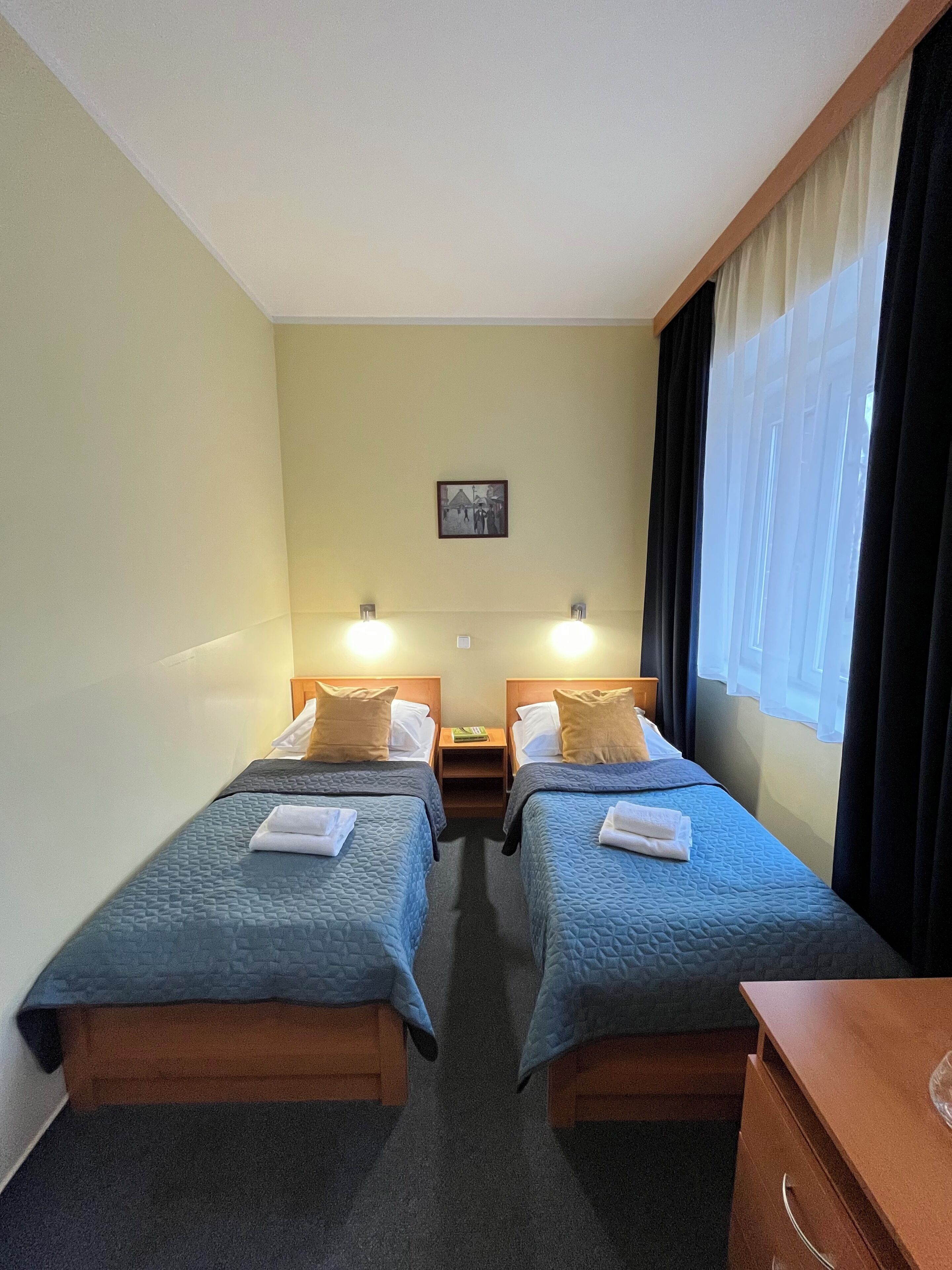 A hotel room with two beds, a nightstand, a small table, and a picture on the wall.