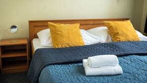 Een net opgemaakt bed met een blauwe sprei, twee kussens en opgevouwen witte handdoeken.