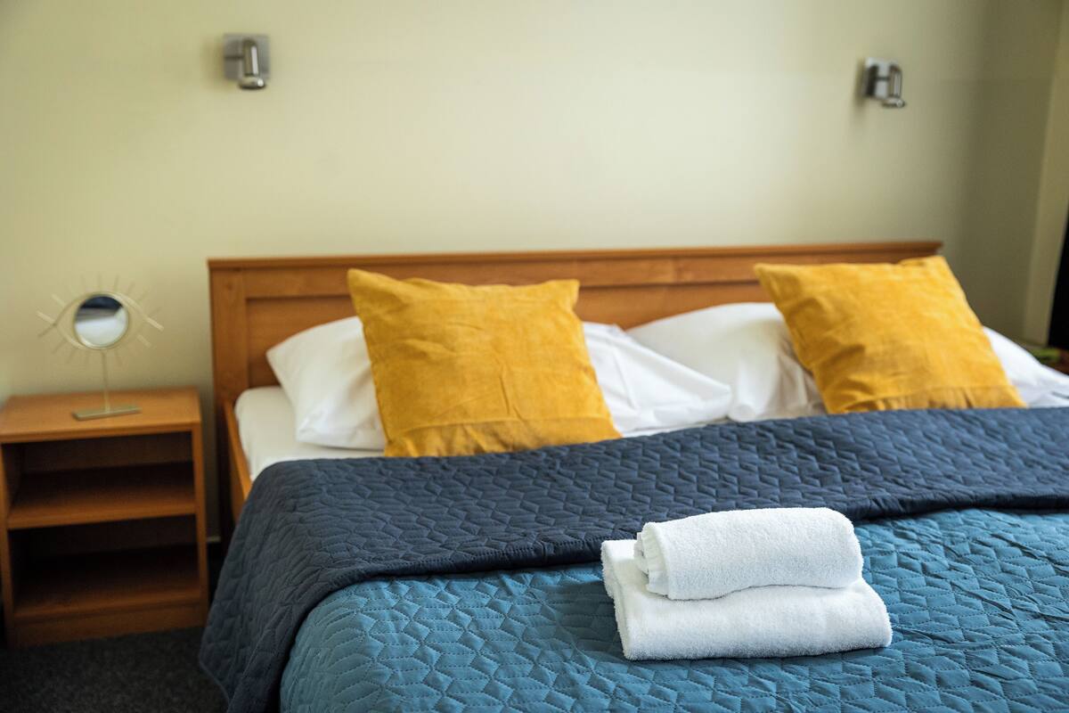 A neatly made bed with a blue quilt, two pillows, and folded white towels.