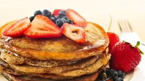 Een stapel pannenkoeken met aardbeien en bosbessen, overgoten met siroop en een vork ernaast.