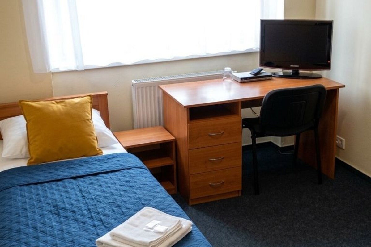 Una habitación de hotel con una cama, un escritorio, una computadora y una ventana con cortinas translúcidas.