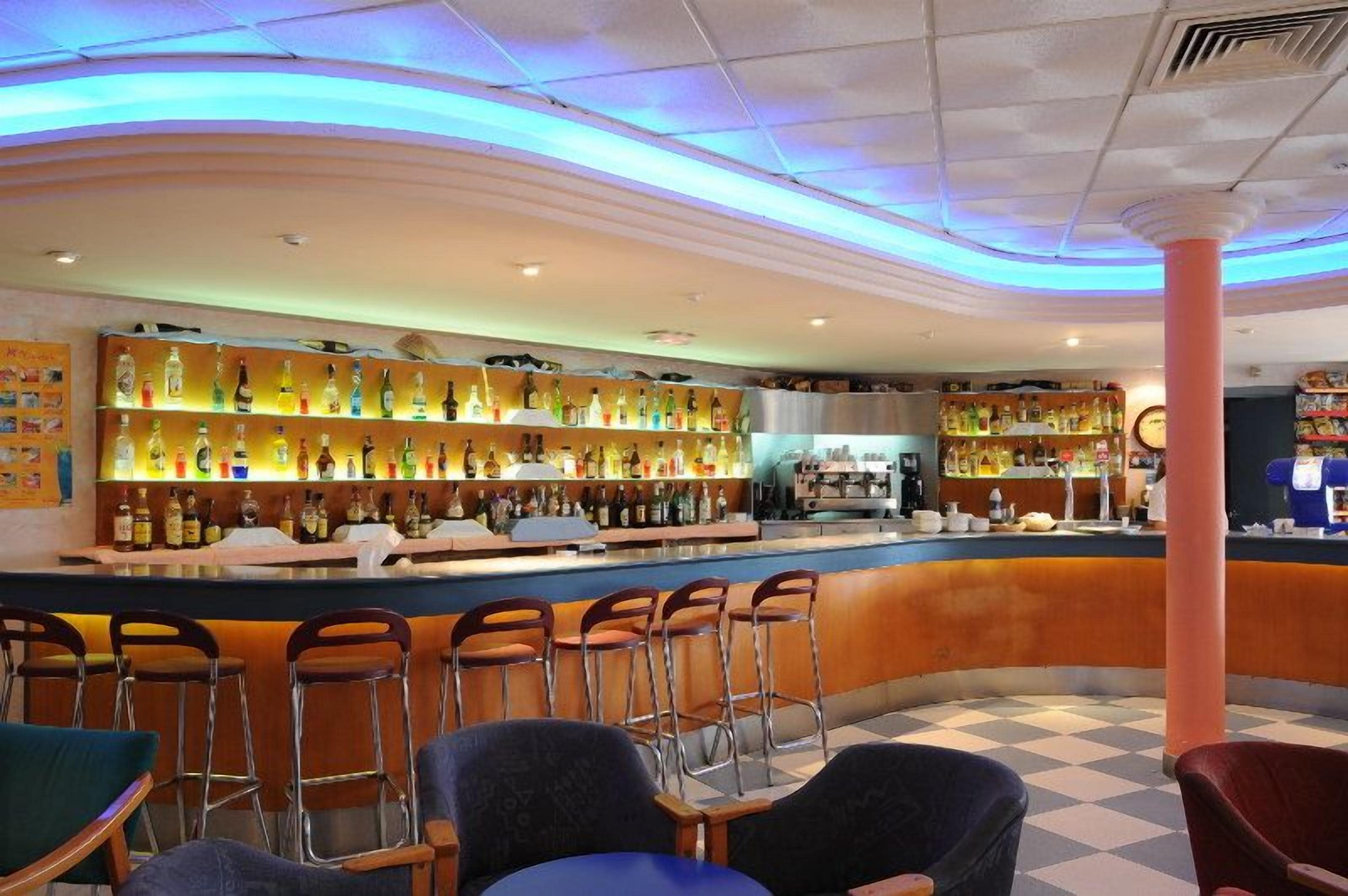 Un área de bar con mostrador, taburetes y estantes llenos de botellas.