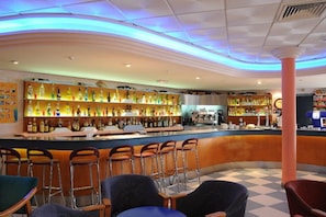 A bar area with a counter, stools, and shelves of bottles. - Alone (Finestrat)