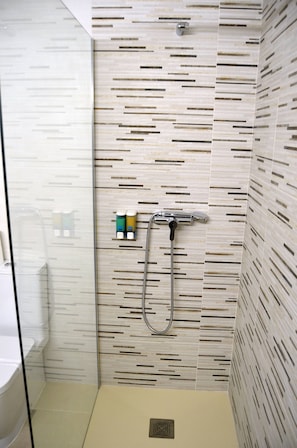 A modern shower with a horizontal water flow design, a glass partition, and a small shelf with toiletries. - Alone (Finestrat)
