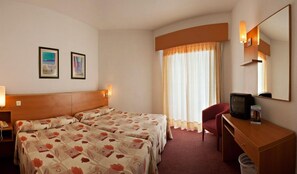 A hotel room with two beds, a desk with a television, a chair, a waste bin, and two framed pictures on the wall. - Alone (Finestrat)
