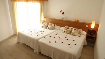 A hotel room with two beds, a nightstand, a lamp, and a window with curtains.