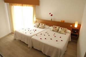 A hotel room with two beds, a nightstand, a lamp, and a window with curtains. - Alone (Finestrat)