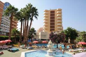 A pool area with lounge chairs, palm trees, and a fountain. - Alone (Finestrat)