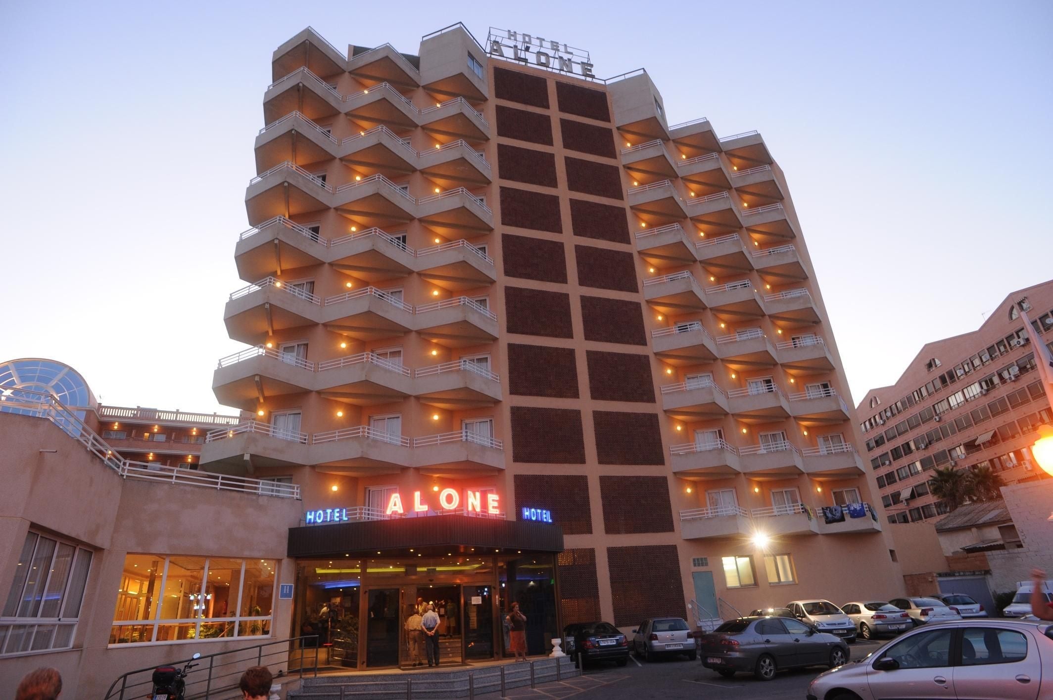 Um hotel com vários andares, varandas, entrada no nível da rua e área de estacionamento.
