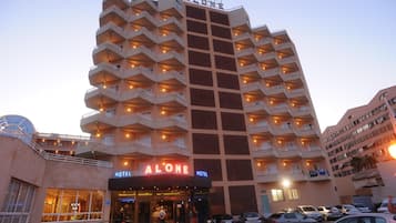 Um hotel com vários andares, varandas, entrada no nível da rua e área de estacionamento.