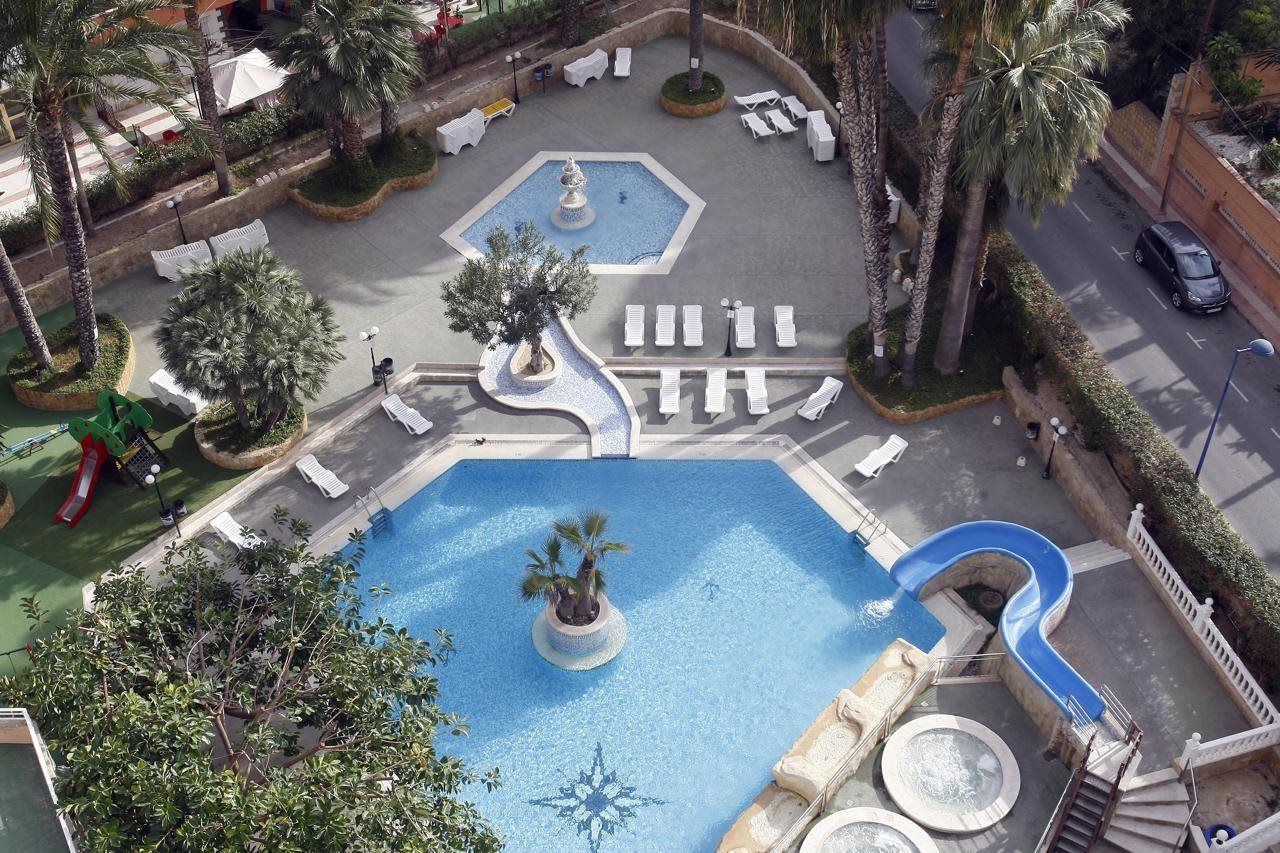Una piscina con fuente, rodeada de sillas de descanso y palmeras.