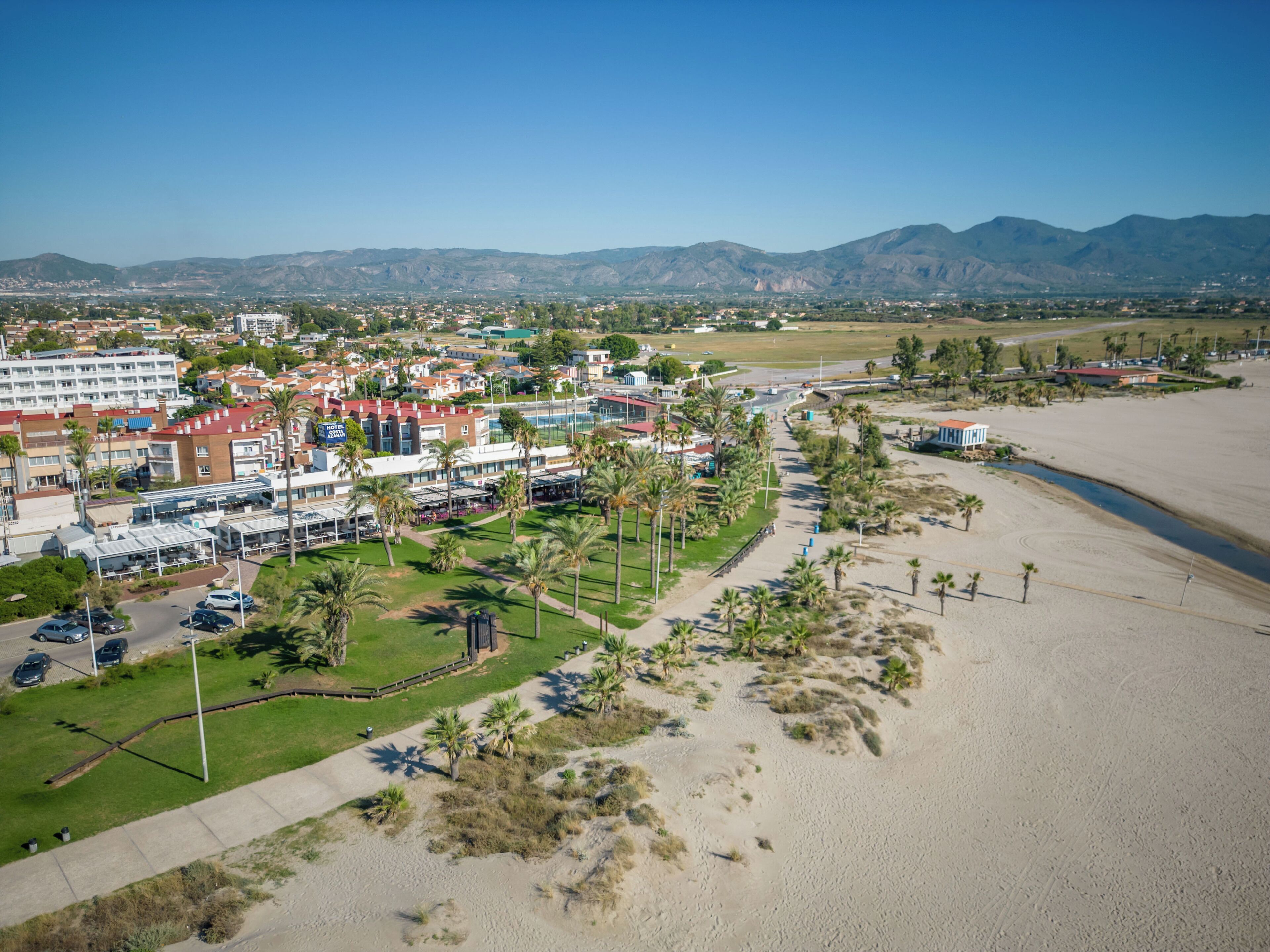 Vista aérea de un complejo turístico costero con playa, palmeras y una variedad de edificios hoteleros.