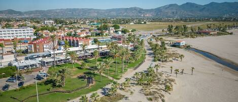 An aerial view of a coastal resort with a beachfront, palm trees, and a mix of hotel buildings.
