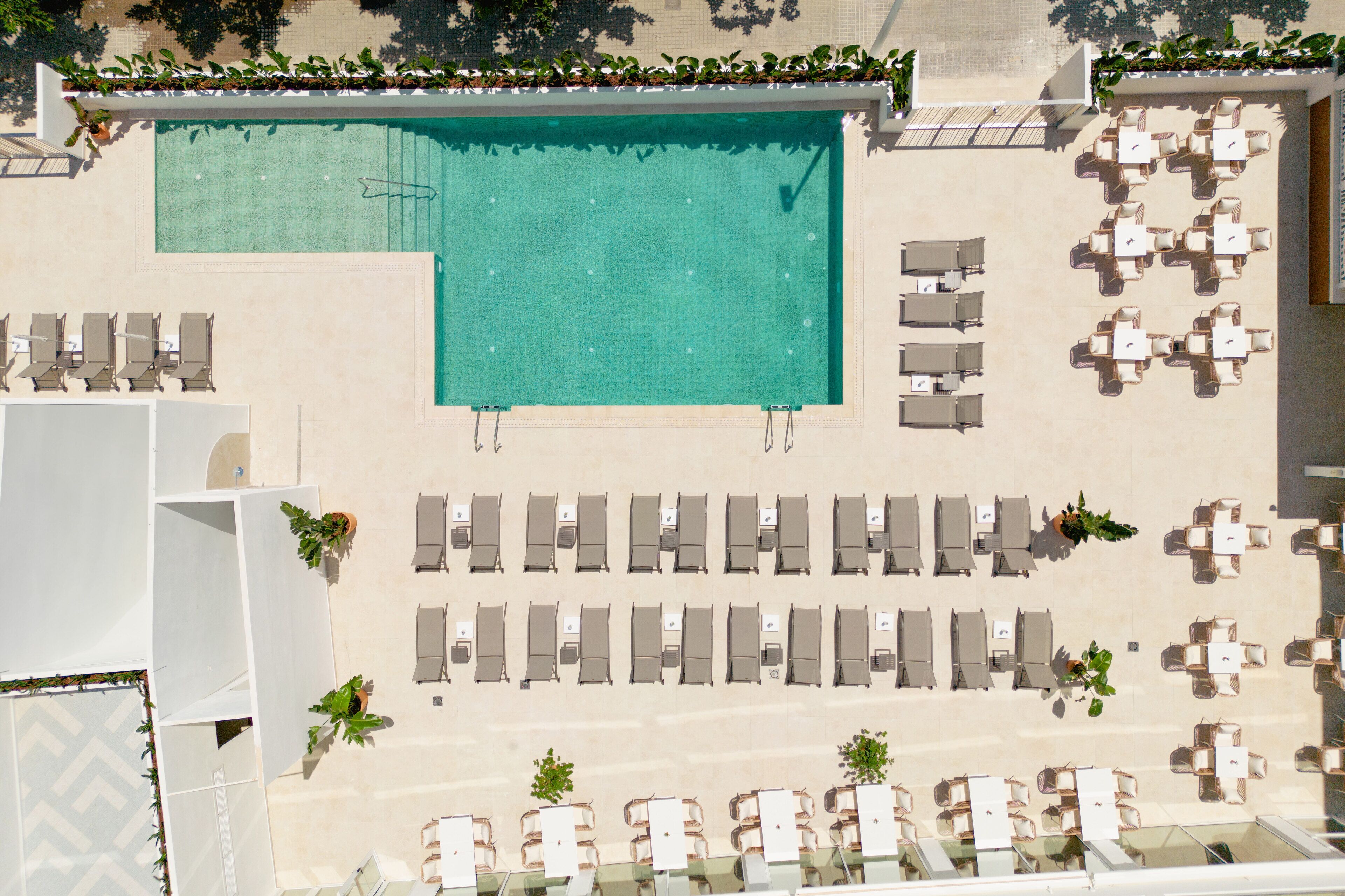 An aerial view of a hotel with a swimming pool, multiple lounge areas with chairs and tables, and a section with a glass balustrade.