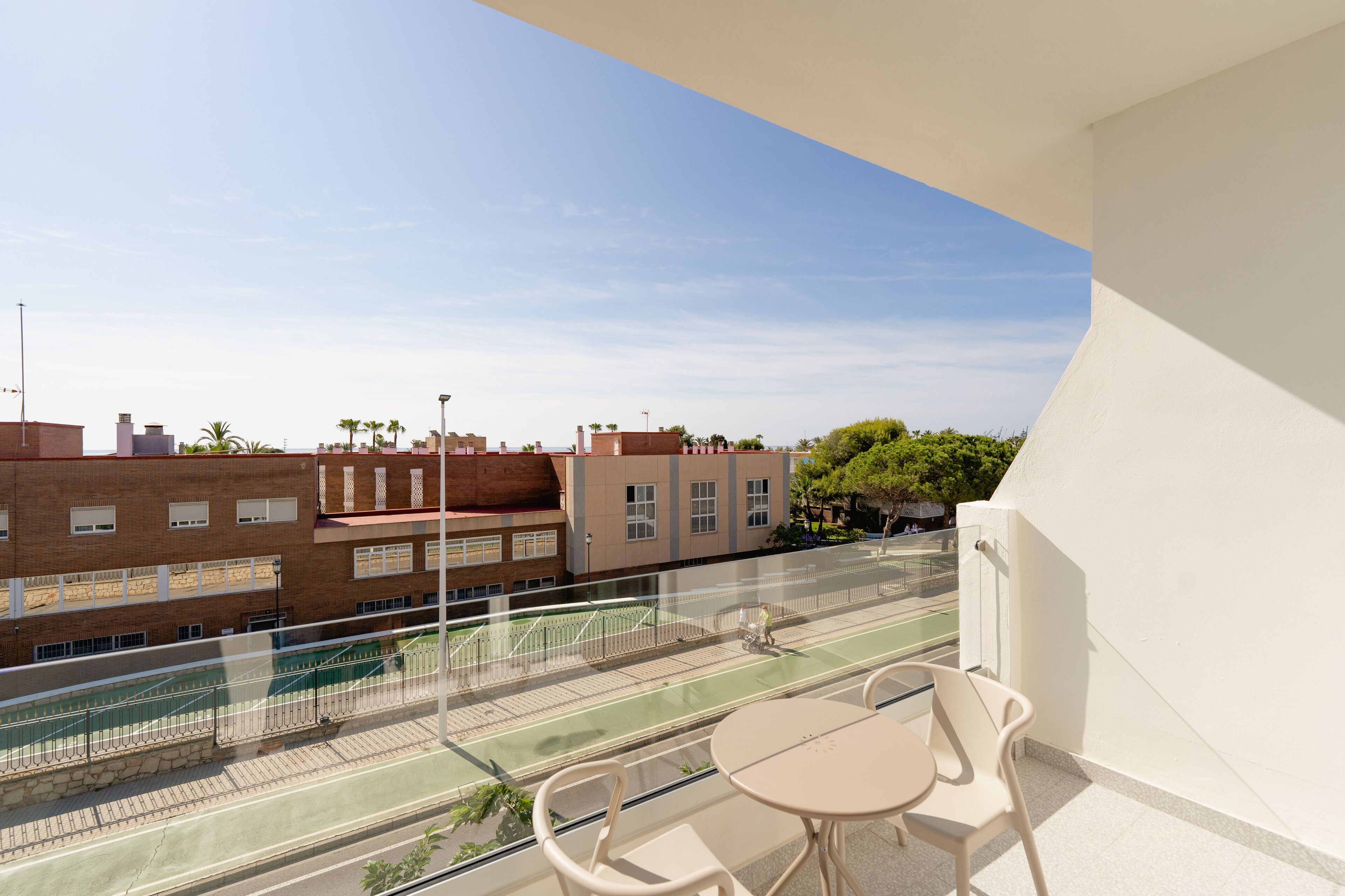 A balcony with a table and chairs, overlooking a tennis court and buildings.
