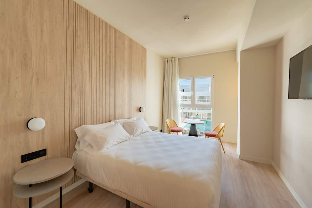 A hotel room with a large bed, a small round table, a chair, a TV, and a balcony with a view.