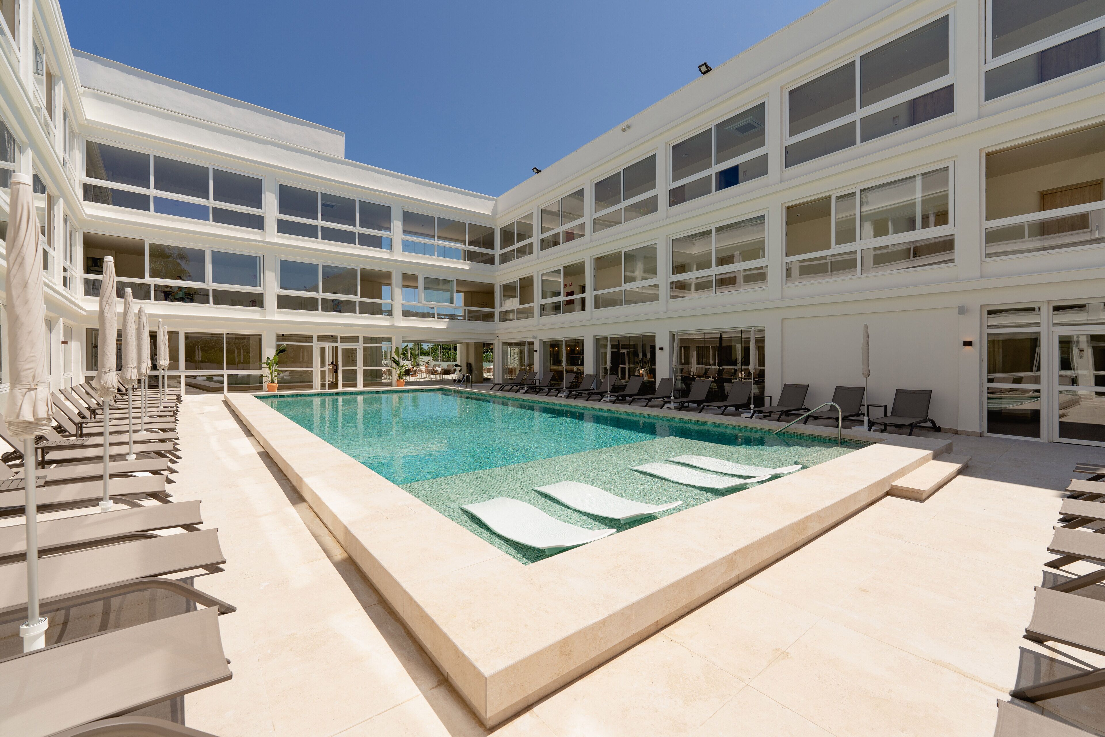 Un hotel moderno con una amplia piscina cubierta, varios balcones y tumbonas.