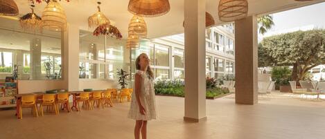 A spacious indoor area with multiple seating arrangements, large windows, and hanging wicker lamps.