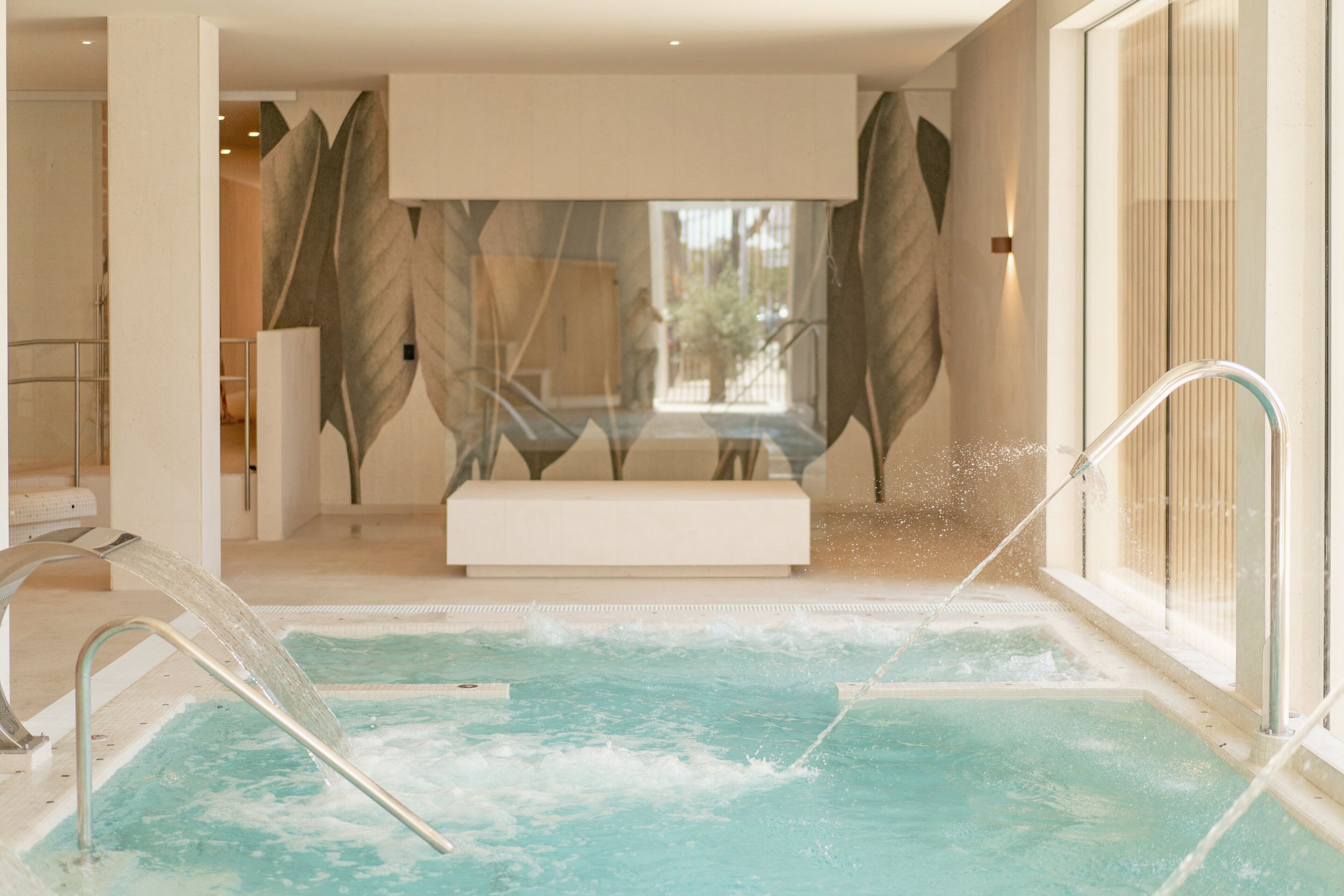 Un área de piscina interior moderna con un banco y una pared de vidrio.