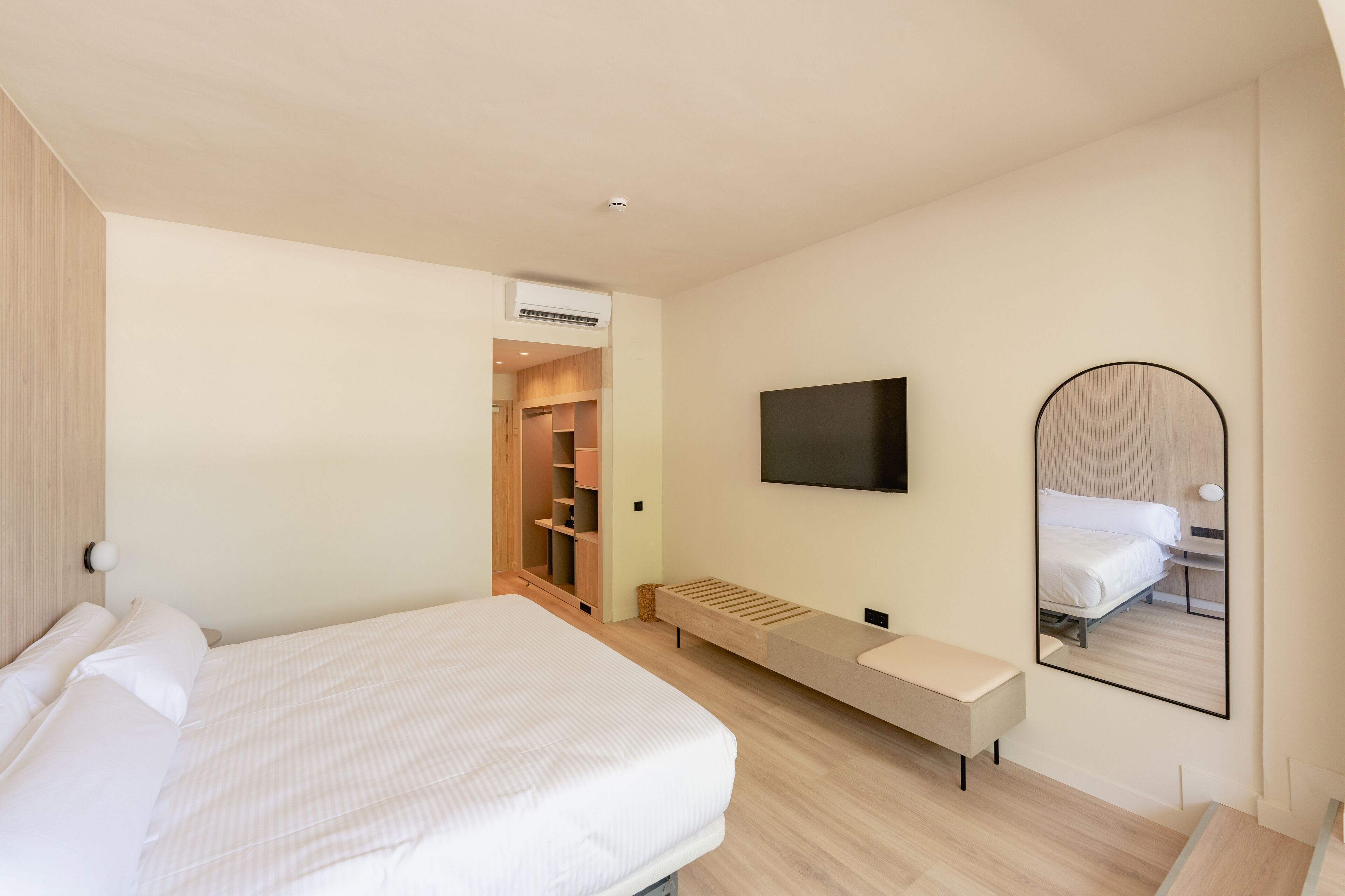 A modern hotel room with a bed, a bench, a TV, and a mirror.