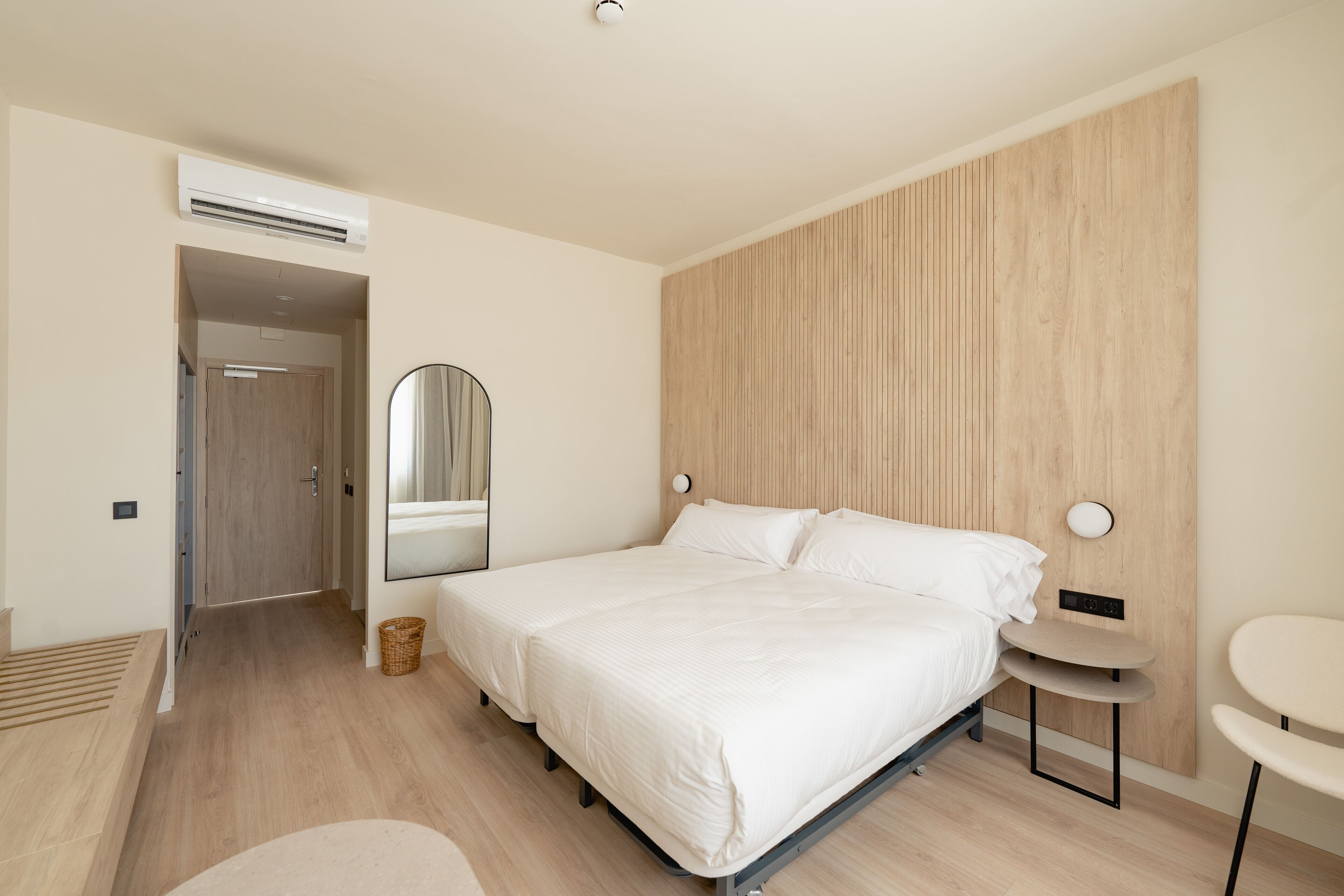 Un dormitorio moderno con una cama grande, una mesita de noche, un espejo y un equipo de aire acondicionado.