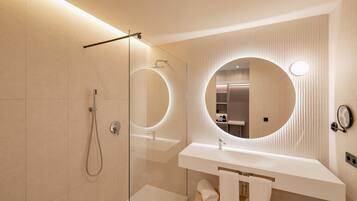 Un baño moderno con ducha envuelta en vidrio, espejo redondo y lavamanos blanco.