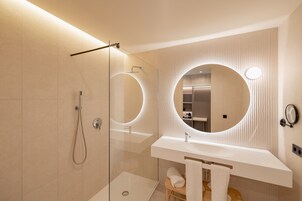 Un baño moderno con ducha envuelta en vidrio, espejo redondo y lavamanos blanco.