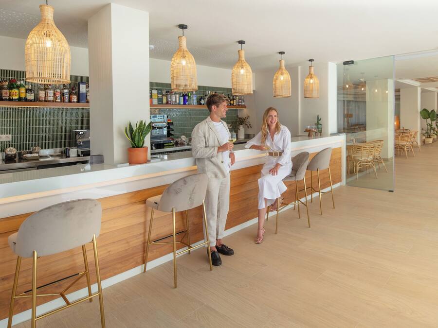 A modern bar area with wooden bar counters, wicker pendant lights, and a glass partition separating the bar from the dining area.