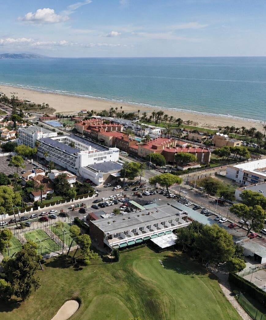 Vista aérea de una zona costera con playa, edificios y un campo de golf.