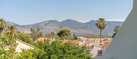 A view of a residential area with mountains in the background, a clear sky, and lush greenery.