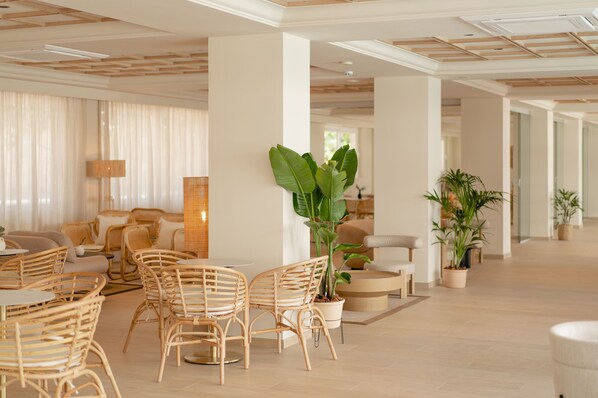 A spacious lobby with wicker furniture, potted plants, and a modern ceiling design.