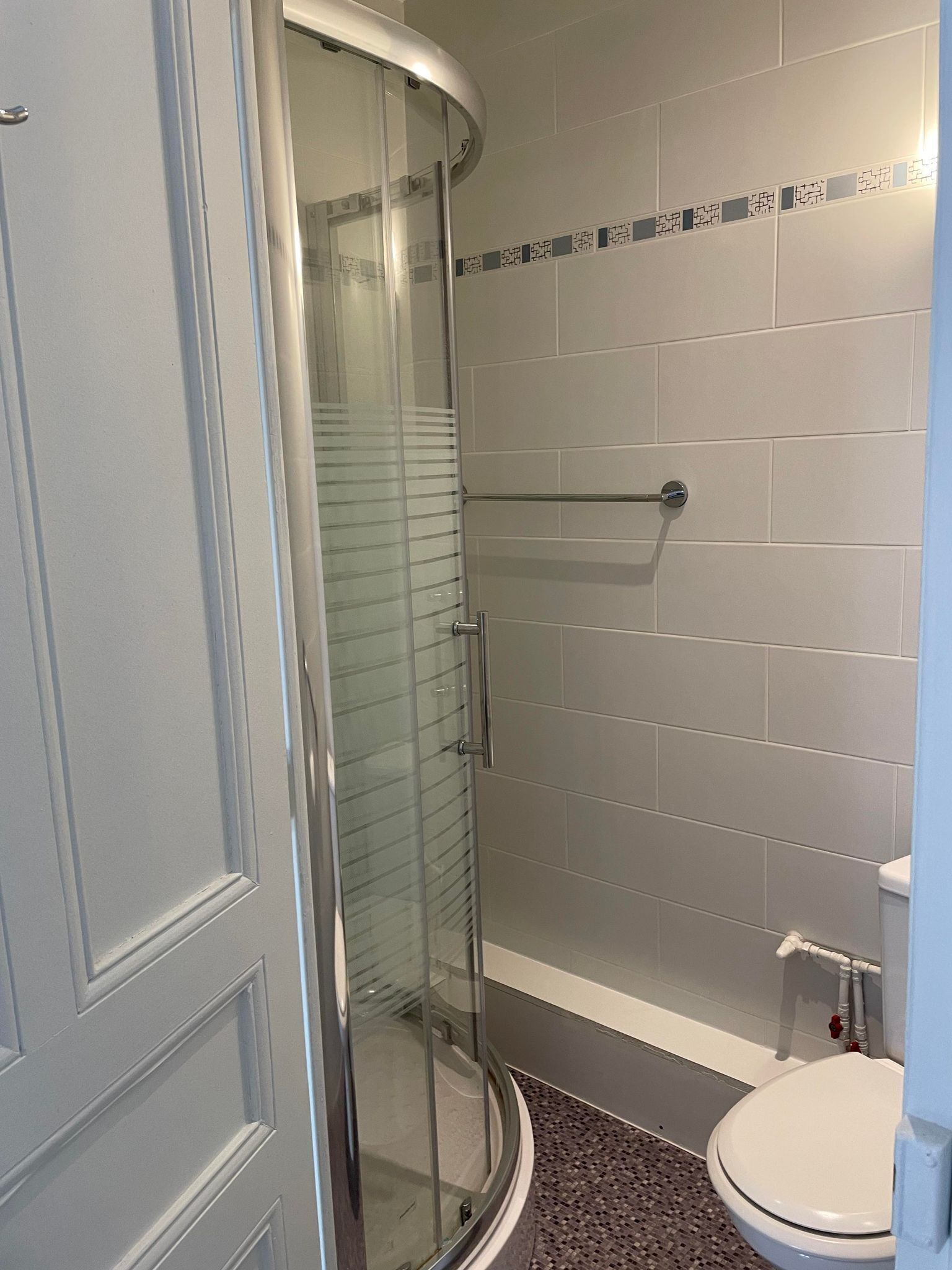 A bathroom with a glass shower enclosure, a toilet, and a tiled wall with a decorative border.