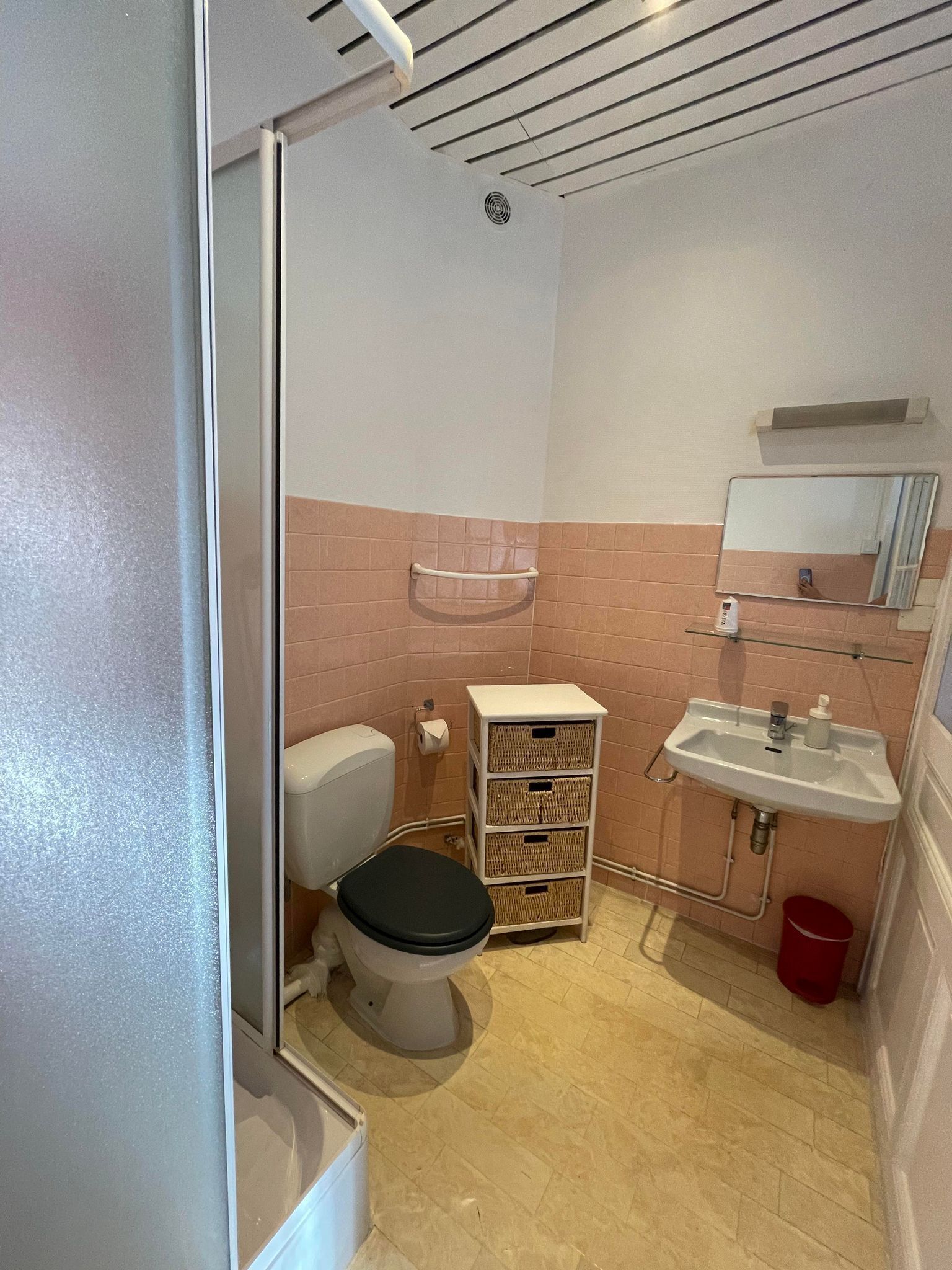 A compact bathroom with a toilet, a sink, a mirror, and a small storage unit.