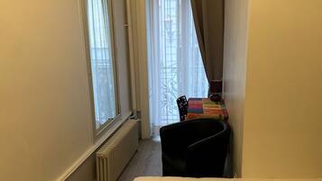A hotel room with a bed, a radiator, a window with curtains, and a chair.