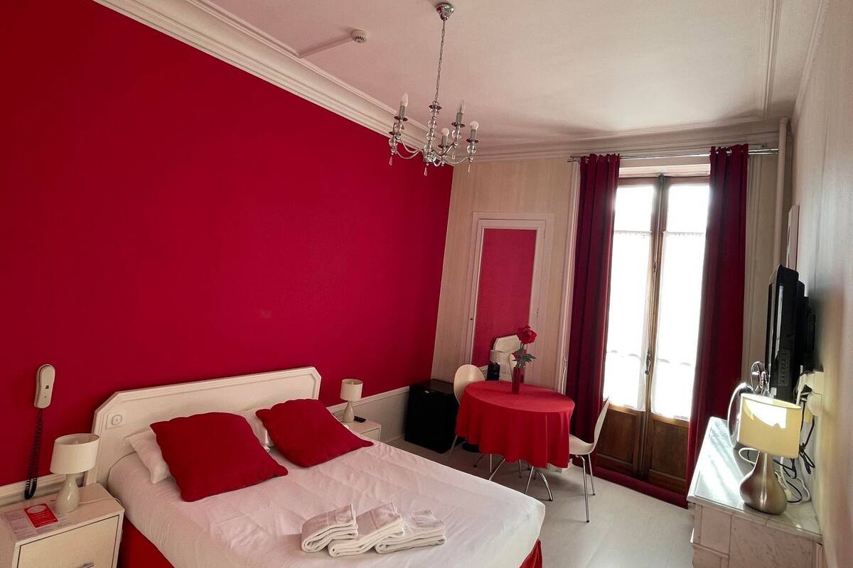 A hotel room with a large bed, a desk, a chair, a small table, and a TV.