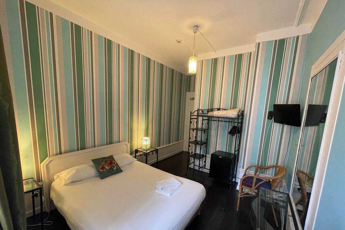 A hotel room with a bed, a small table with a lamp, a bunk bed, and a chair.