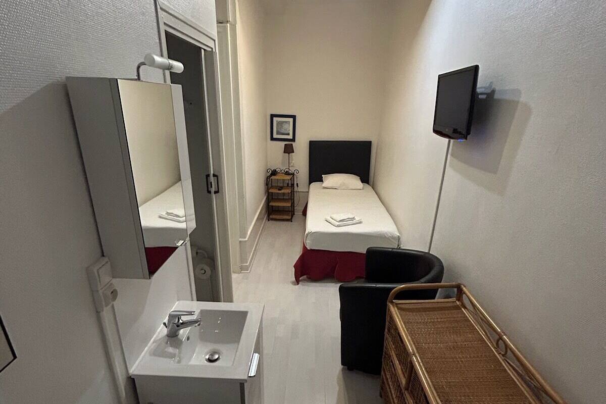 A compact hotel room with a bed, bedside table, mirror, TV, and a small desk with a sink.