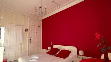 A bedroom with a large bed, red walls, a chandelier, and a table with a vase.