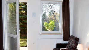 Une pièce comprenant un lit, une chaise, une fenêtre avec des stores, un radiateur et une vue sur les arbres et l’herbe à l’extérieur.