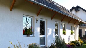 Une maison à deux étages, avec une façade blanche, de nombreuses fenêtres et un toit en pente.