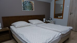 Un lit double avec une literie blanche et une tête de lit en bois, une table de chevet avec une lampe et un miroir fixé au mur.
