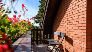 Une terrasse avec un mur en briques, une balustrade en bois et deux chaises en métal.