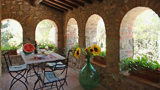 A rustic stone patio with a table set for dining, surrounded by arched brick walls and potted plants. - Casale Aronne (Massa Marittima)